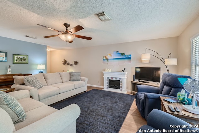 living room with ceiling fan, a textured ceiling, light wood-type flooring, and a tiled fireplace