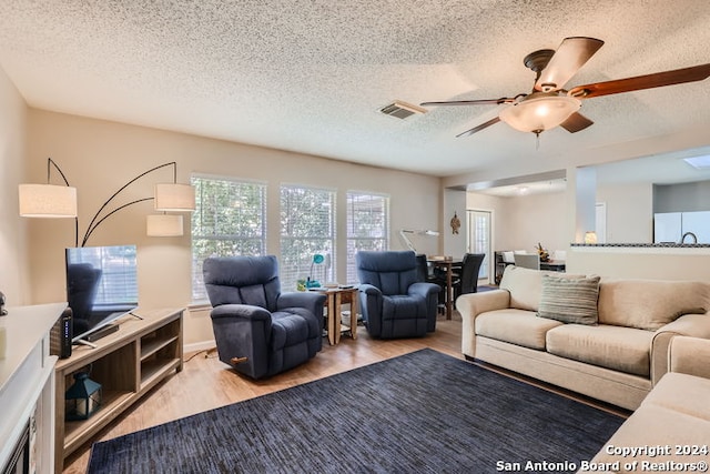 living room with ceiling fan, a textured ceiling, and light wood-type flooring