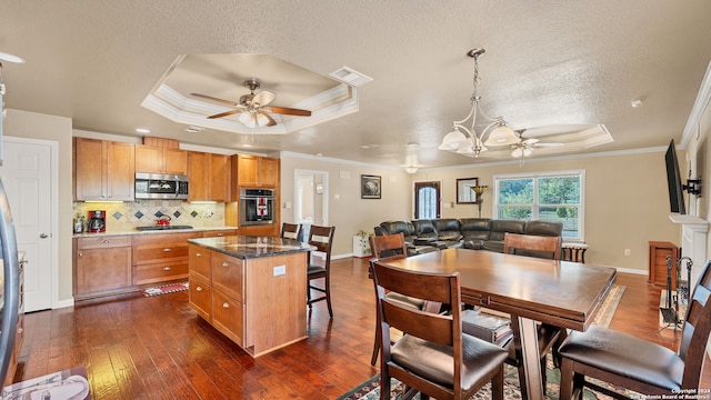 kitchen featuring appliances with stainless steel finishes, a tray ceiling, a kitchen island, and dark wood-type flooring