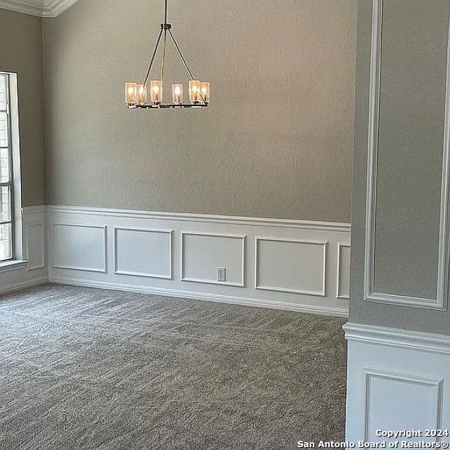 carpeted spare room featuring a notable chandelier and crown molding