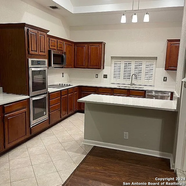 kitchen featuring sink, backsplash, appliances with stainless steel finishes, light tile patterned floors, and decorative light fixtures