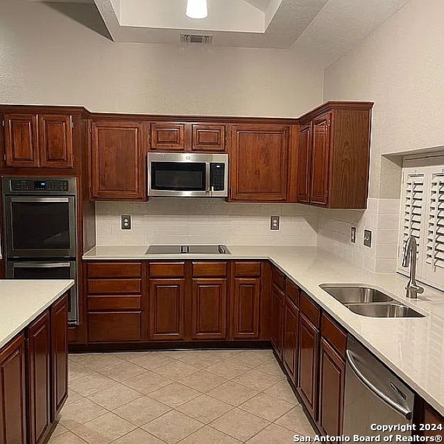 kitchen featuring appliances with stainless steel finishes, sink, light tile patterned floors, and tasteful backsplash