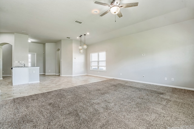 carpeted empty room featuring ceiling fan with notable chandelier