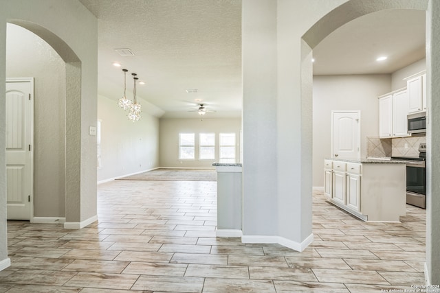 kitchen featuring light stone counters, ceiling fan with notable chandelier, appliances with stainless steel finishes, and white cabinetry