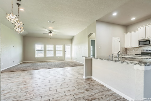 kitchen featuring ceiling fan, pendant lighting, white cabinets, appliances with stainless steel finishes, and dark stone counters