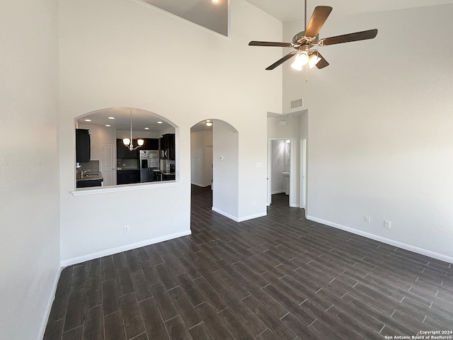 unfurnished living room with ceiling fan, sink, a towering ceiling, and dark wood-type flooring