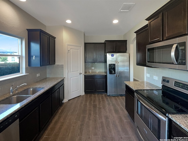 kitchen with decorative backsplash, dark wood-type flooring, light stone countertops, stainless steel appliances, and sink