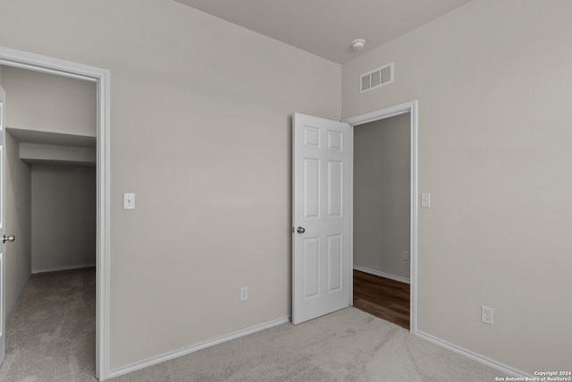 unfurnished bedroom with light carpet and a walk in closet