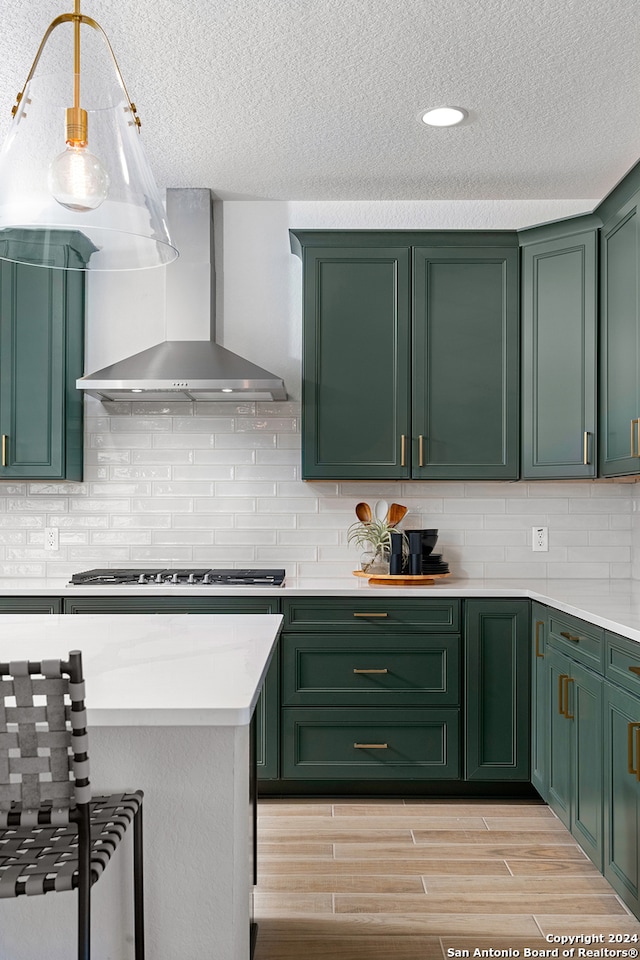 kitchen featuring decorative backsplash, wall chimney exhaust hood, green cabinetry, stainless steel gas cooktop, and light hardwood / wood-style flooring