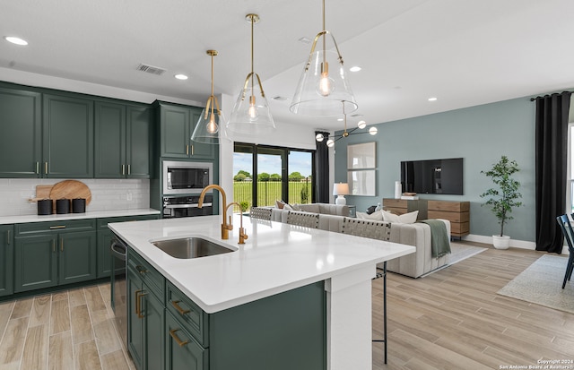 kitchen featuring an island with sink, green cabinets, light hardwood / wood-style floors, and sink