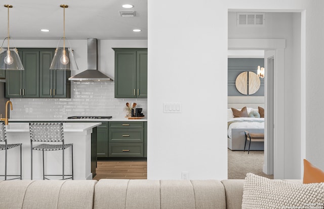 kitchen featuring green cabinetry, hanging light fixtures, dark wood-type flooring, and wall chimney range hood