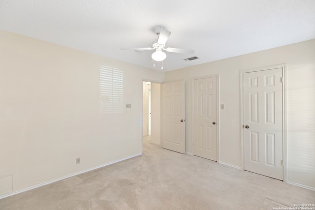 unfurnished bedroom featuring light carpet, two closets, and ceiling fan