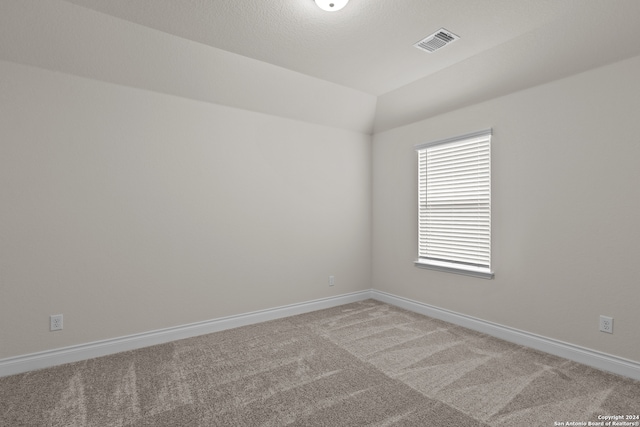 carpeted spare room with a textured ceiling and vaulted ceiling