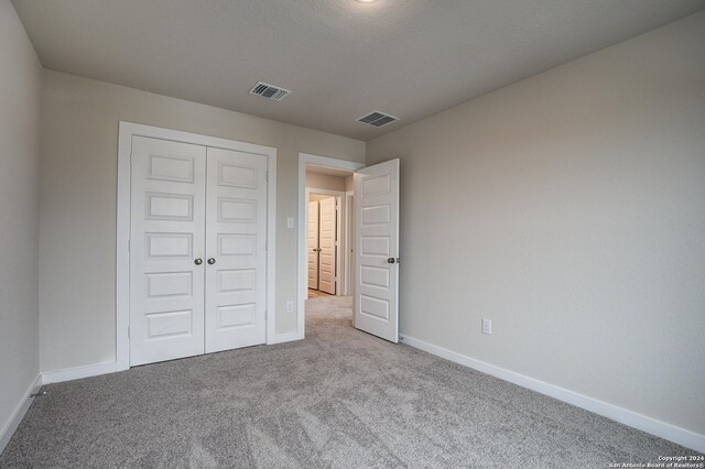 unfurnished bedroom featuring light carpet, a textured ceiling, and a closet