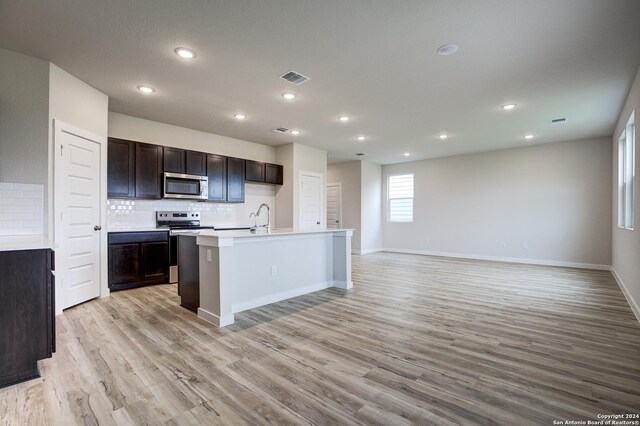 kitchen with sink, stainless steel appliances, light hardwood / wood-style flooring, and an island with sink