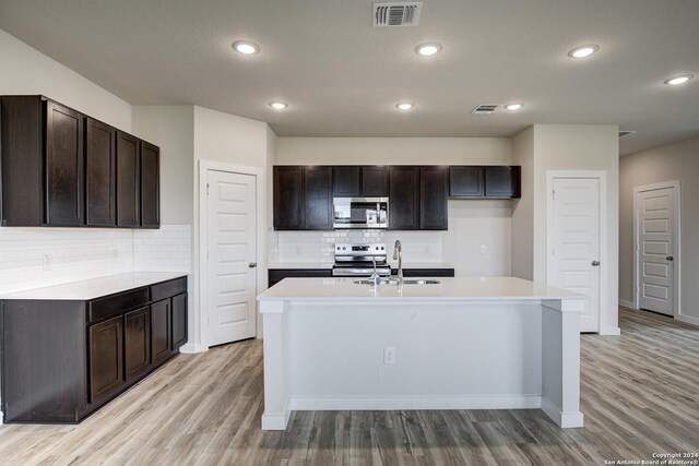 kitchen with light wood-type flooring, sink, appliances with stainless steel finishes, and an island with sink