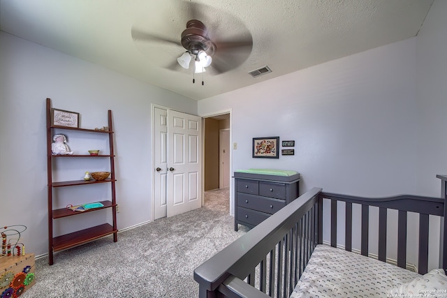 carpeted bedroom featuring a closet, ceiling fan, a crib, and a textured ceiling