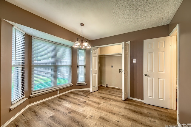 unfurnished bedroom with a textured ceiling, an inviting chandelier, light hardwood / wood-style flooring, and a closet