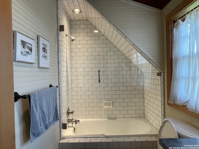 bathroom with tiled shower / bath combo, wooden walls, and toilet