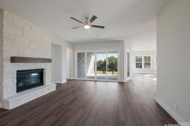 unfurnished living room with a stone fireplace, dark hardwood / wood-style floors, a healthy amount of sunlight, and ceiling fan with notable chandelier