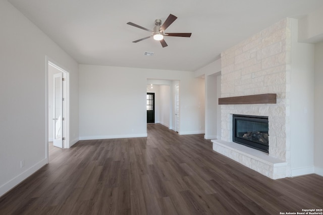 unfurnished living room featuring ceiling fan, a stone fireplace, and dark wood-type flooring