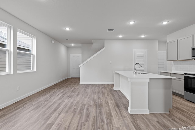 kitchen with gray cabinetry, stainless steel appliances, a kitchen island with sink, sink, and light hardwood / wood-style flooring