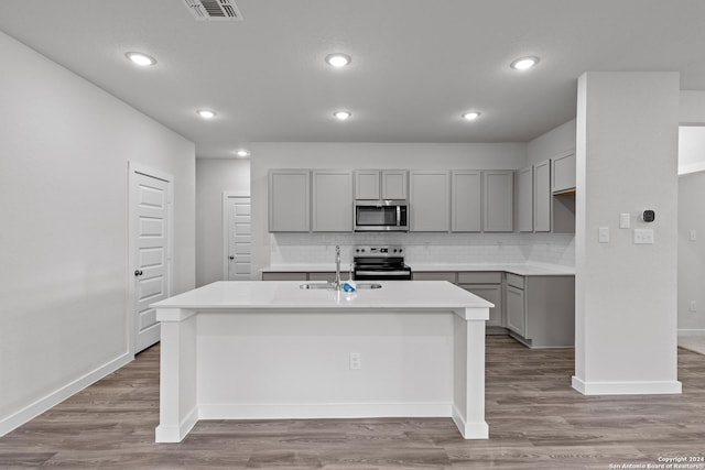 kitchen featuring gray cabinetry, tasteful backsplash, light hardwood / wood-style flooring, a kitchen island with sink, and appliances with stainless steel finishes