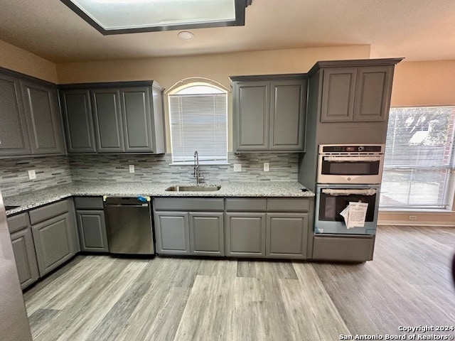 kitchen with light stone counters, sink, tasteful backsplash, appliances with stainless steel finishes, and light hardwood / wood-style floors