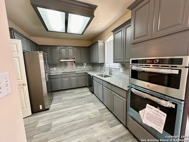 kitchen featuring sink, tasteful backsplash, gray cabinetry, light hardwood / wood-style flooring, and appliances with stainless steel finishes