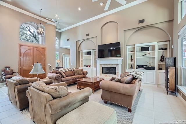 tiled living room with ceiling fan with notable chandelier, a high end fireplace, a high ceiling, and crown molding