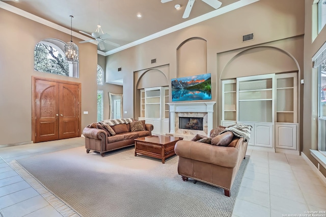 living area featuring crown molding, ceiling fan with notable chandelier, a fireplace, a towering ceiling, and visible vents