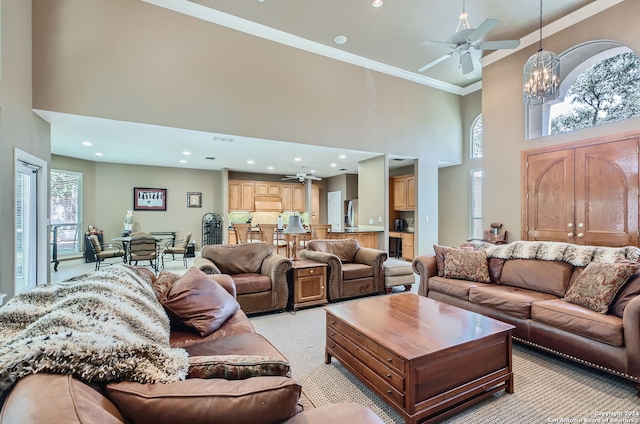 living room featuring a towering ceiling, ceiling fan with notable chandelier, ornamental molding, and light carpet