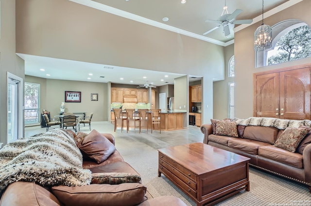 living room featuring ornamental molding, a towering ceiling, light carpet, and ceiling fan with notable chandelier