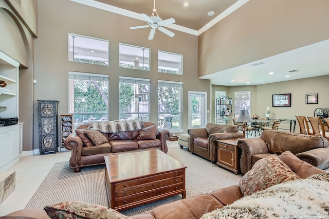 living room featuring light tile patterned flooring, built in shelves, ceiling fan, crown molding, and a towering ceiling