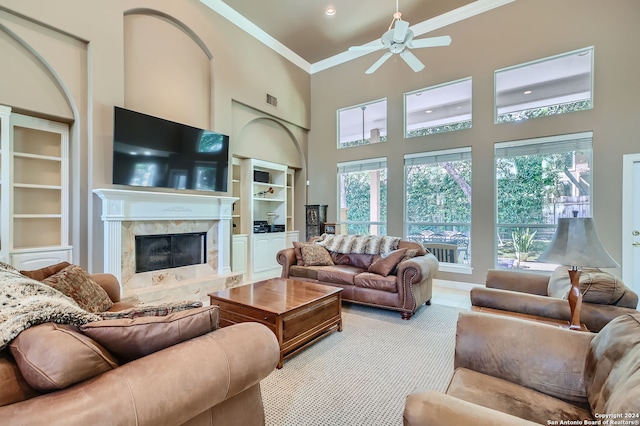 living room with ceiling fan, built in shelves, a high ceiling, a fireplace, and crown molding