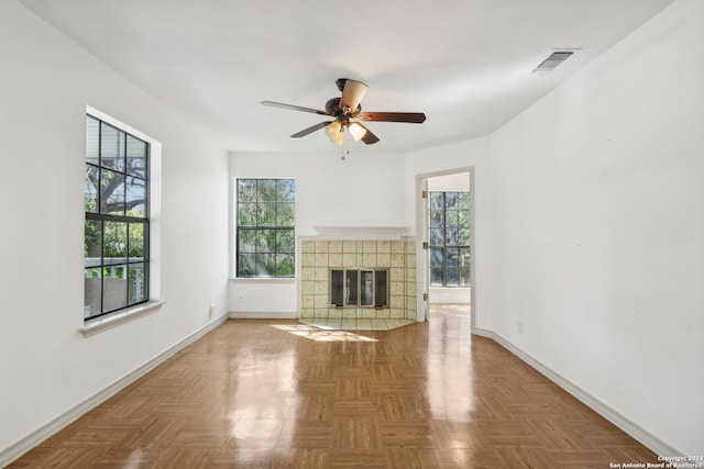 unfurnished living room with ceiling fan, parquet flooring, a tile fireplace, and a healthy amount of sunlight