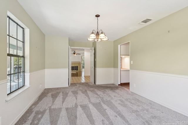 carpeted spare room with ceiling fan with notable chandelier