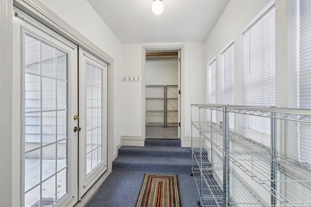 hallway featuring french doors, dark colored carpet, and a wealth of natural light