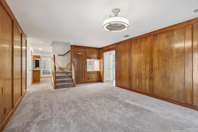 unfurnished living room featuring wood walls and light colored carpet