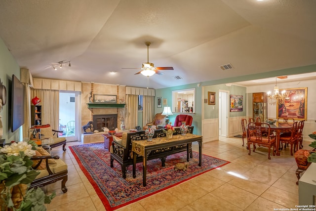 tiled dining space with a textured ceiling, a stone fireplace, lofted ceiling, and ceiling fan with notable chandelier