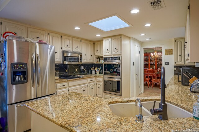 kitchen with light stone countertops, appliances with stainless steel finishes, a skylight, and a notable chandelier