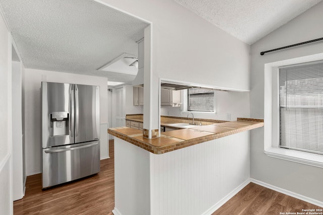 kitchen featuring hardwood / wood-style floors, vaulted ceiling, kitchen peninsula, stainless steel refrigerator with ice dispenser, and a textured ceiling