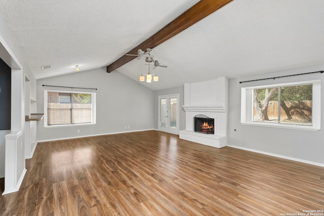 unfurnished living room featuring ceiling fan, vaulted ceiling with beams, a textured ceiling, a fireplace, and hardwood / wood-style floors