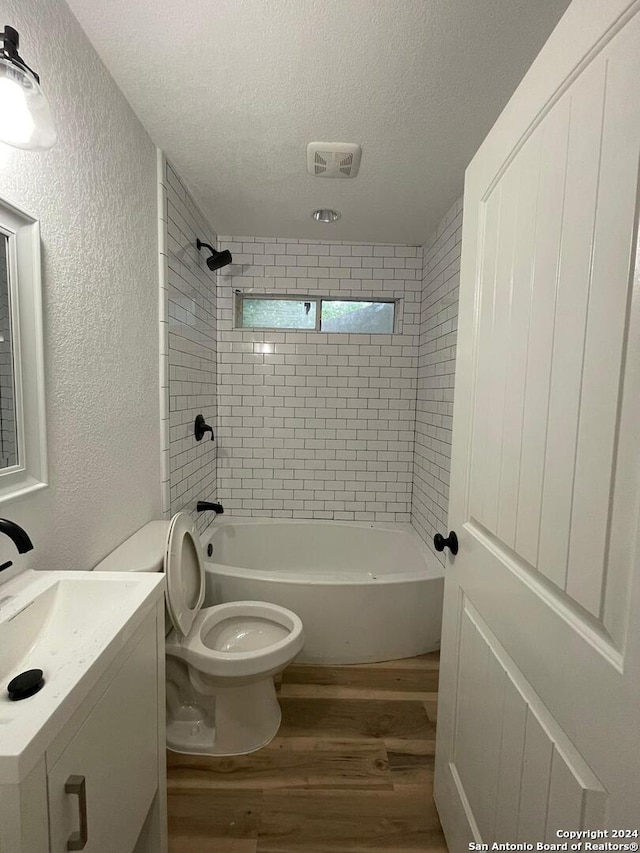 full bathroom featuring tiled shower / bath, vanity, a textured ceiling, hardwood / wood-style flooring, and toilet