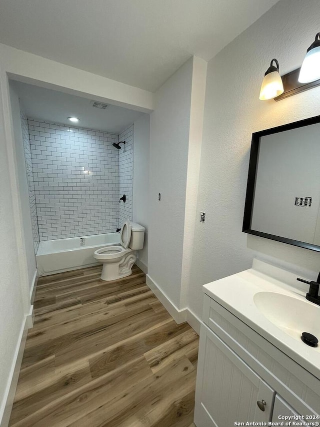 full bathroom with tiled shower / bath, hardwood / wood-style flooring, vanity, and toilet