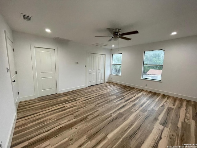 unfurnished bedroom featuring hardwood / wood-style flooring, ceiling fan, and two closets