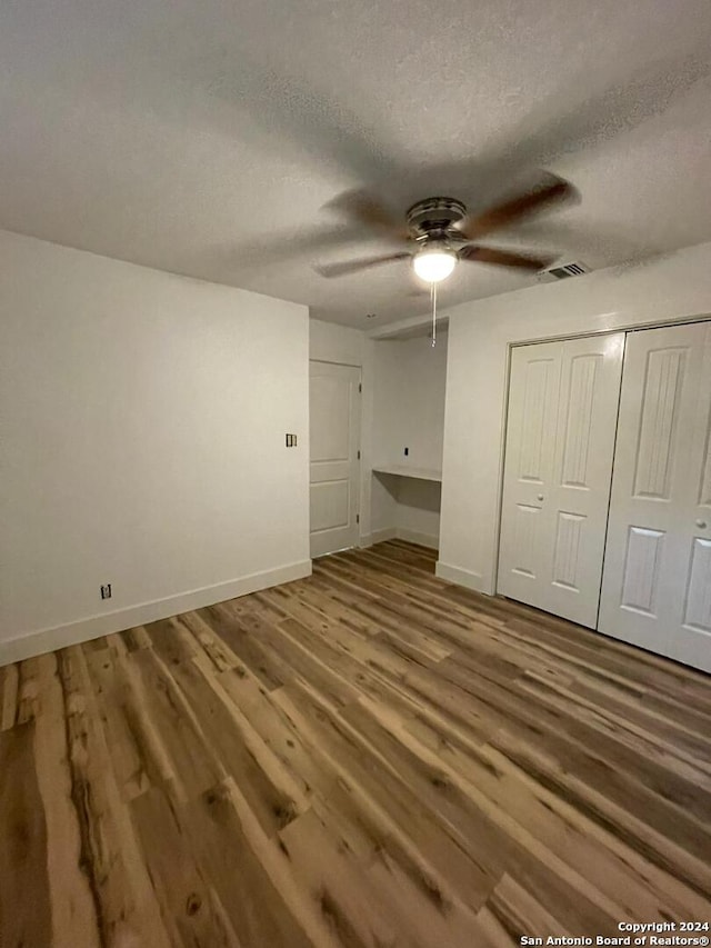 unfurnished bedroom featuring a closet, hardwood / wood-style flooring, a textured ceiling, and ceiling fan