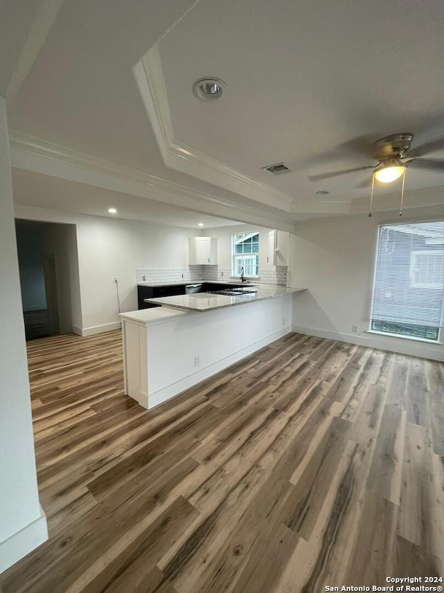 kitchen with kitchen peninsula, crown molding, wood-type flooring, and white cabinetry