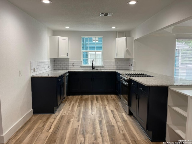 kitchen with light wood-type flooring, sink, kitchen peninsula, stainless steel gas range, and white cabinetry