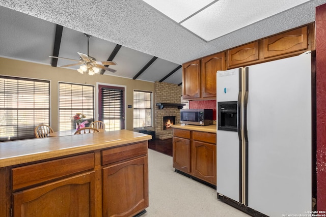 kitchen with a brick fireplace, a textured ceiling, ceiling fan, vaulted ceiling with beams, and white fridge with ice dispenser